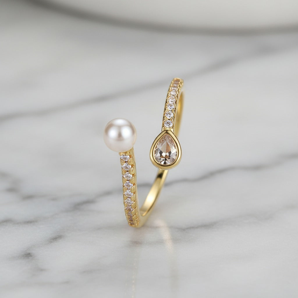 Gold ring with a pearl and teardrop-shaped gemstone on a marble background