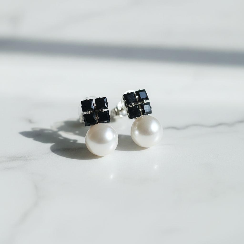 Pearl earrings with black geometric accents on a marble surface