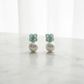 Pair of earrings with pearl-like centers and teal gemstones on a white background