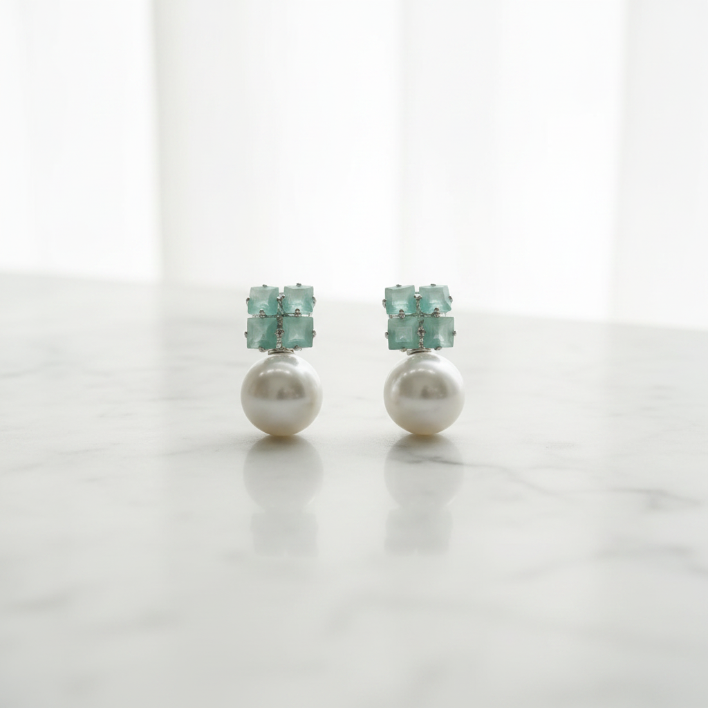 Pair of earrings with pearl-like centers and teal gemstones on a white background